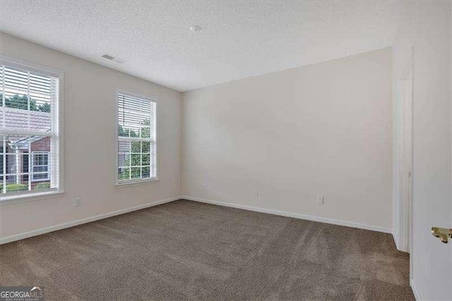 spare room featuring dark carpet, a textured ceiling, and a wealth of natural light