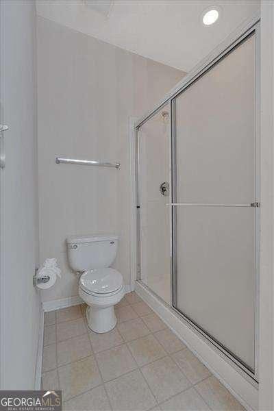 bathroom with tile patterned floors, toilet, and a shower with shower door