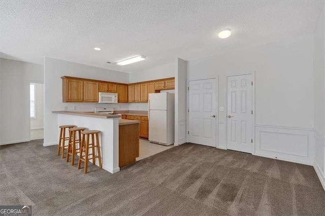 kitchen featuring white appliances, light colored carpet, kitchen peninsula, and a kitchen bar