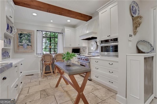 kitchen featuring appliances with stainless steel finishes, beamed ceiling, white cabinets, backsplash, and custom range hood