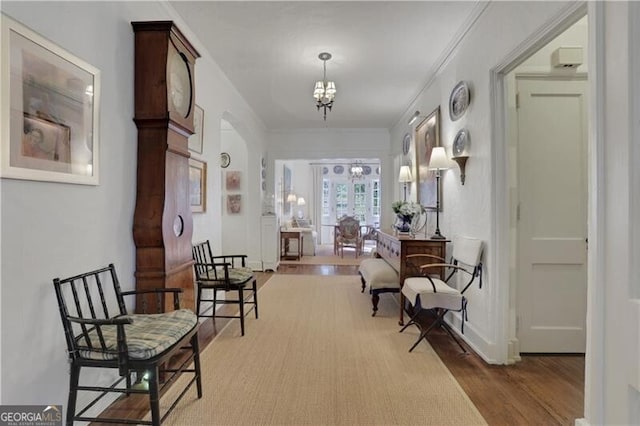 hallway featuring wood-type flooring, ornamental molding, and a chandelier