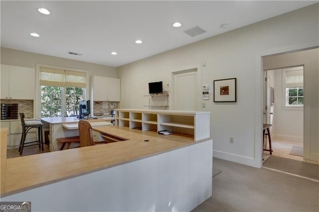 kitchen with a kitchen breakfast bar, tasteful backsplash, white cabinets, light carpet, and kitchen peninsula