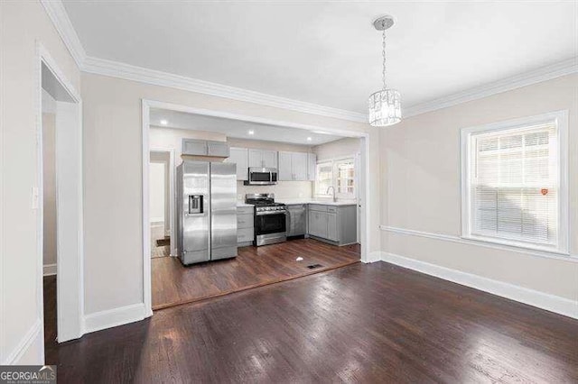 kitchen featuring dark wood-type flooring, ornamental molding, appliances with stainless steel finishes, and hanging light fixtures