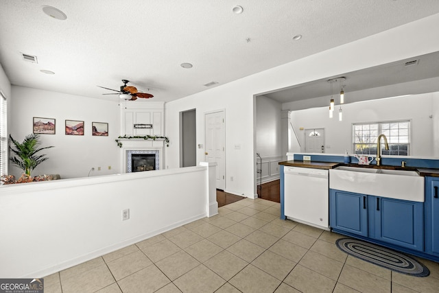 kitchen featuring visible vents, dishwasher, a glass covered fireplace, blue cabinetry, and a sink