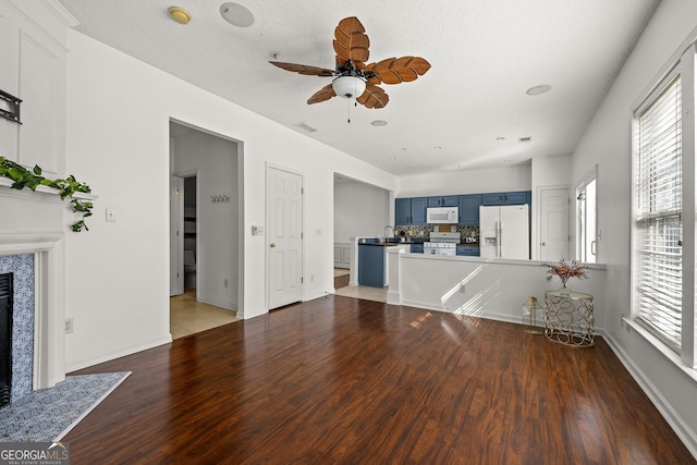 unfurnished living room with dark wood-style floors, plenty of natural light, a ceiling fan, and a tiled fireplace