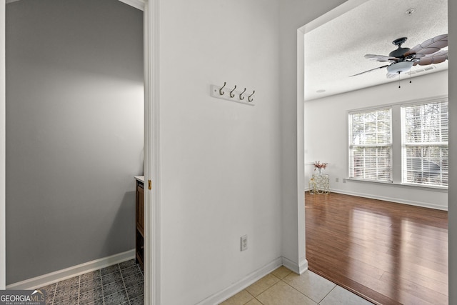 interior space with a textured ceiling, light tile patterned floors, a ceiling fan, and baseboards