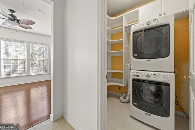 washroom with a ceiling fan, a textured ceiling, baseboards, and stacked washer / drying machine