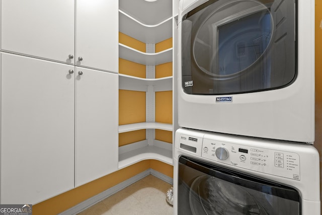 laundry room with stacked washer / dryer, cabinet space, and baseboards