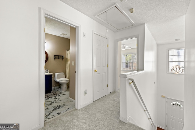 hallway with a textured ceiling, light carpet, an upstairs landing, baseboards, and attic access