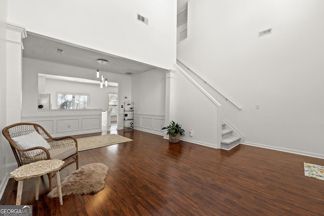 living area with dark wood-style floors, stairway, visible vents, and ornate columns