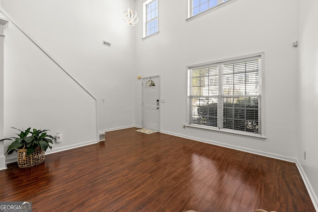 foyer with visible vents, a towering ceiling, baseboards, and wood finished floors