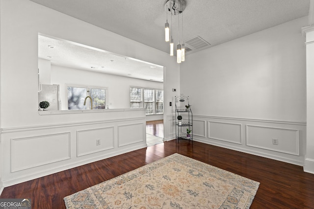 dining room with dark wood-style floors, a textured ceiling, wainscoting, and a decorative wall