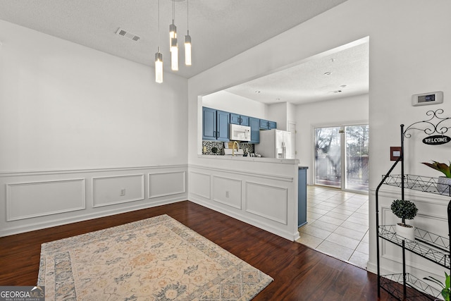 kitchen with white microwave, blue cabinets, visible vents, refrigerator with ice dispenser, and light countertops