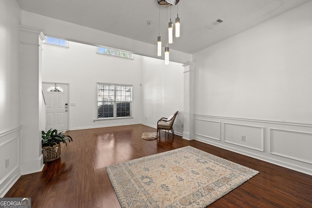 sitting room with visible vents, dark wood-style flooring, decorative columns, and a decorative wall