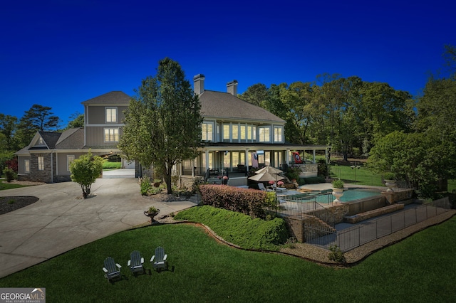 back of property featuring concrete driveway, a lawn, a patio, and a pool with connected hot tub