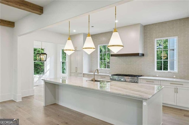 kitchen with an island with sink, custom range hood, sink, and hanging light fixtures