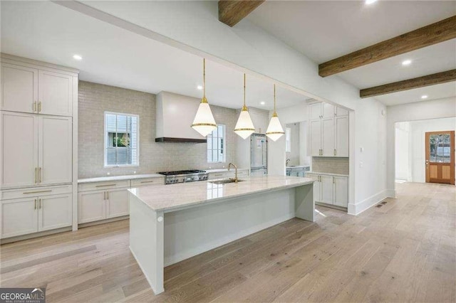 kitchen featuring light hardwood / wood-style flooring, a kitchen island with sink, hanging light fixtures, light stone counters, and custom exhaust hood