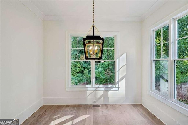 unfurnished dining area featuring an inviting chandelier, crown molding, and wood-type flooring