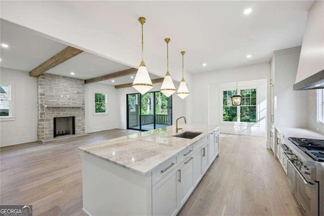 kitchen with sink, premium range hood, white cabinetry, hanging light fixtures, and a kitchen island with sink