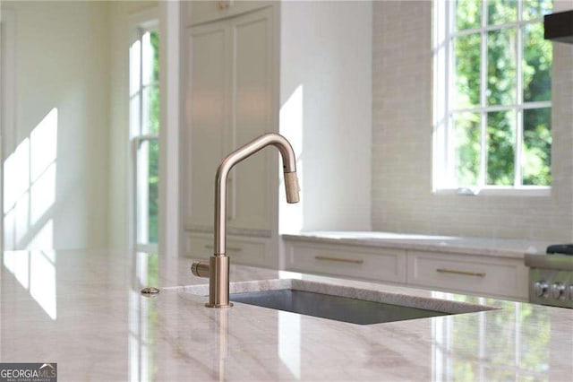 room details featuring sink, white cabinets, and light stone counters