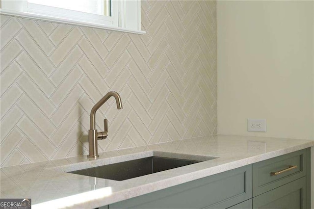 interior details featuring sink, green cabinets, backsplash, and light stone counters