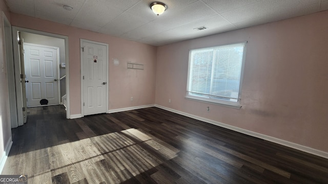 spare room featuring a drop ceiling and dark hardwood / wood-style flooring