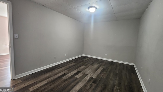 empty room with a drop ceiling and dark wood-type flooring