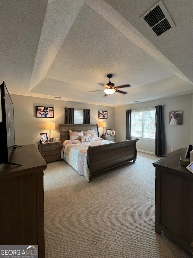 bedroom featuring ceiling fan, light carpet, a textured ceiling, and a tray ceiling