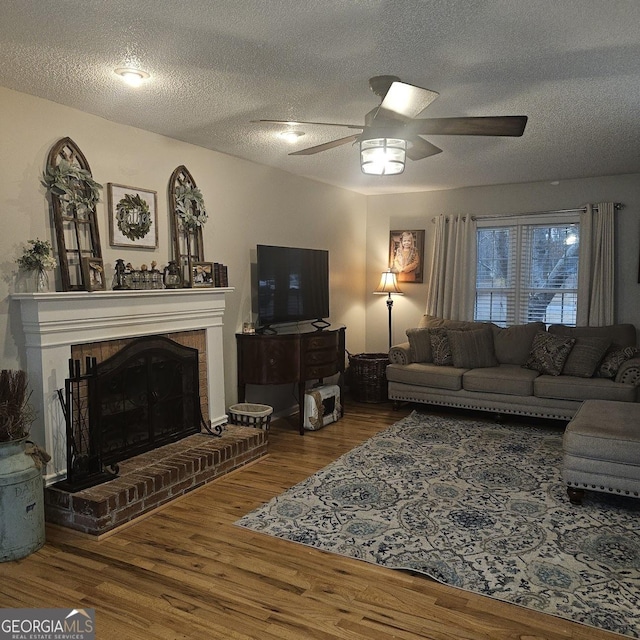 living room with hardwood / wood-style flooring, ceiling fan, a fireplace, and a textured ceiling