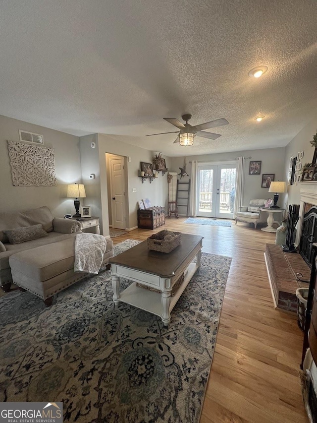 living room featuring french doors, ceiling fan, light hardwood / wood-style floors, and a textured ceiling