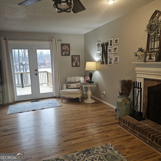 sitting room with hardwood / wood-style flooring, ceiling fan, a textured ceiling, a brick fireplace, and french doors