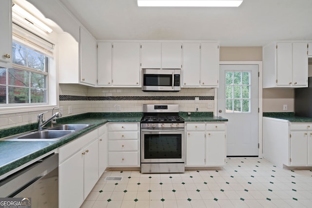 kitchen with stainless steel appliances, a sink, white cabinets, and dark countertops