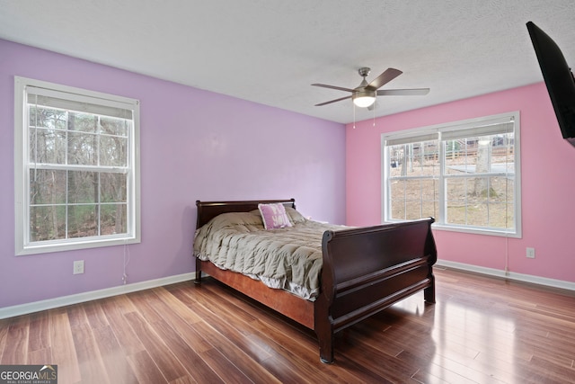 bedroom featuring baseboards, wood finished floors, multiple windows, and a ceiling fan