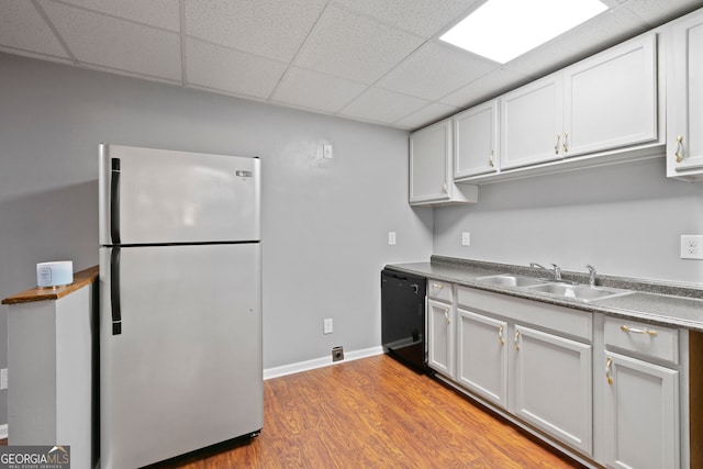 kitchen featuring freestanding refrigerator, black dishwasher, a sink, a drop ceiling, and light wood-style floors