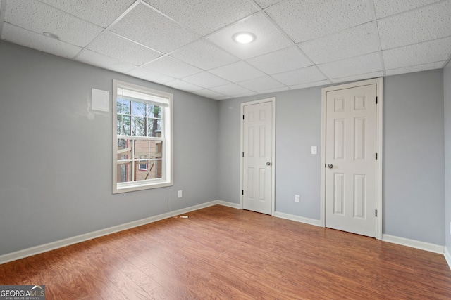 unfurnished bedroom with a drop ceiling, wood finished floors, and baseboards