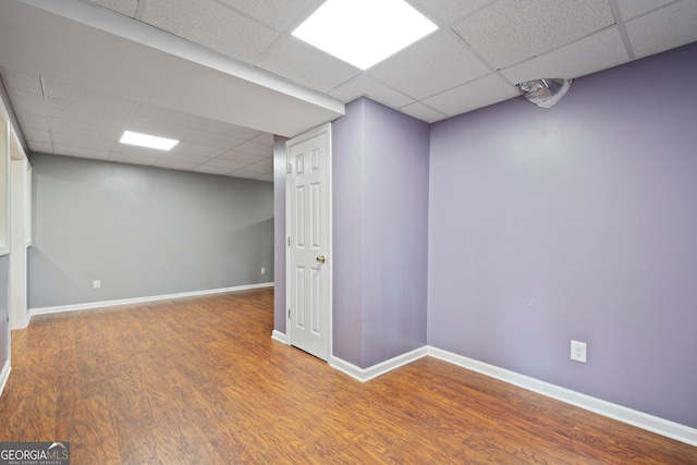 finished below grade area featuring a paneled ceiling, wood finished floors, and baseboards