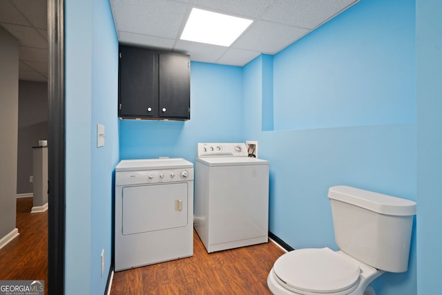 clothes washing area with washing machine and dryer, wood finished floors, and baseboards