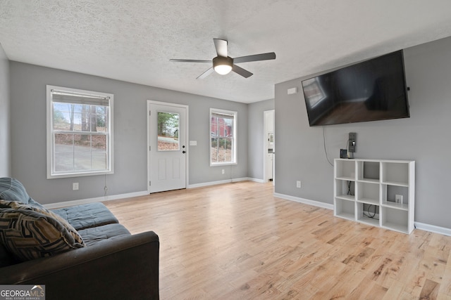 living area with a ceiling fan, light wood-type flooring, healthy amount of natural light, baseboards, and a textured ceiling