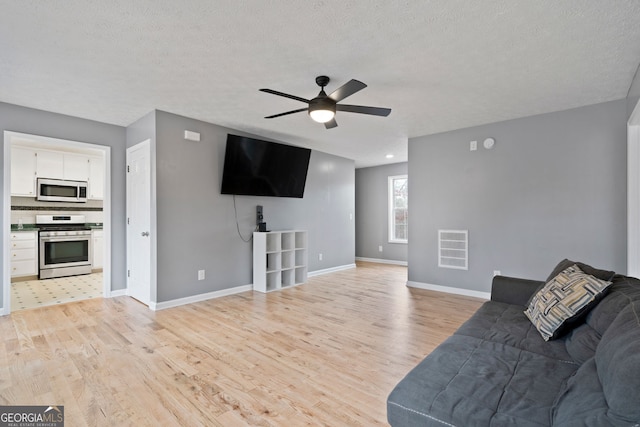 living room featuring light wood-style flooring, ceiling fan, baseboards, and a textured ceiling