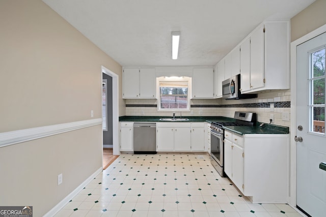 kitchen with appliances with stainless steel finishes, a sink, dark countertops, tasteful backsplash, and white cabinetry