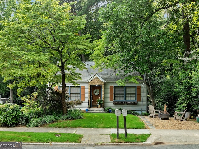 bungalow-style house featuring a front lawn and an outdoor fire pit