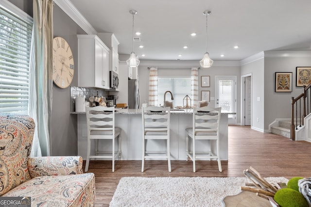 kitchen featuring appliances with stainless steel finishes, light stone countertops, white cabinets, a kitchen bar, and decorative light fixtures