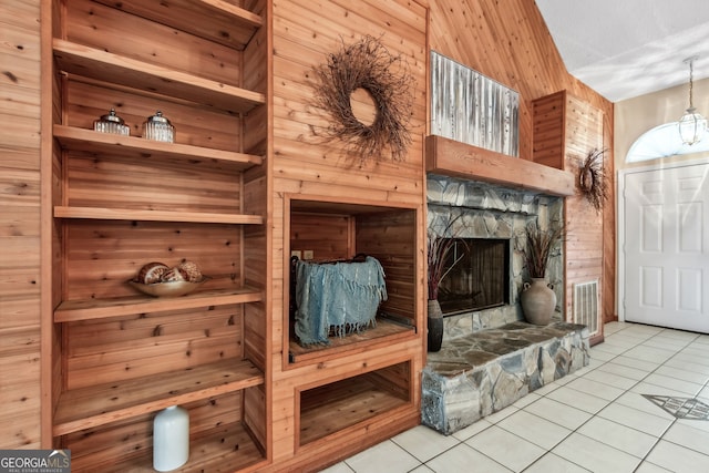 interior space featuring a stone fireplace, light tile patterned floors, and wood walls