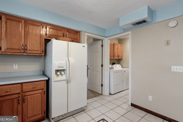 kitchen featuring washer and dryer, white fridge with ice dispenser, light tile patterned floors, and a textured ceiling