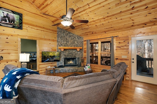 living room featuring hardwood / wood-style flooring, ceiling fan, high vaulted ceiling, a fireplace, and wood walls