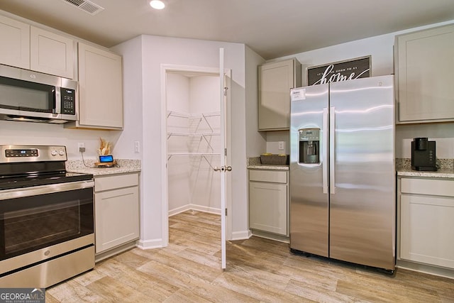 kitchen featuring light stone countertops, appliances with stainless steel finishes, white cabinets, and light wood-type flooring