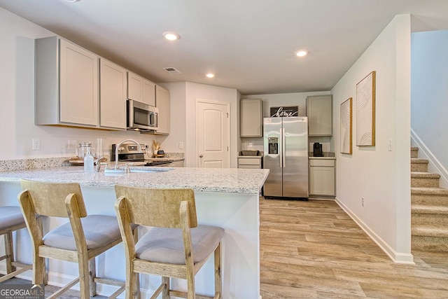 kitchen with sink, a breakfast bar area, light stone counters, appliances with stainless steel finishes, and light hardwood / wood-style floors