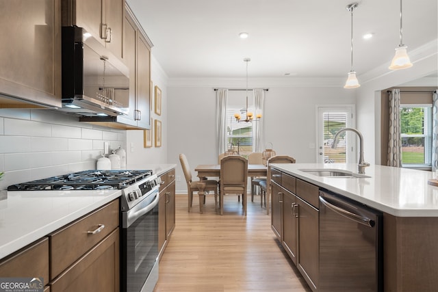 kitchen with pendant lighting, sink, ornamental molding, stainless steel appliances, and a center island with sink