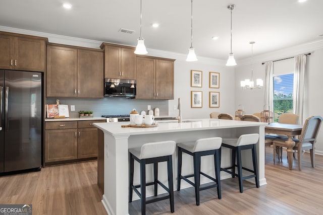 kitchen featuring appliances with stainless steel finishes, pendant lighting, sink, ornamental molding, and a center island with sink