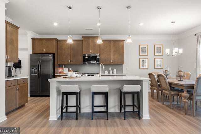 kitchen featuring appliances with stainless steel finishes, decorative light fixtures, a kitchen breakfast bar, crown molding, and a center island with sink